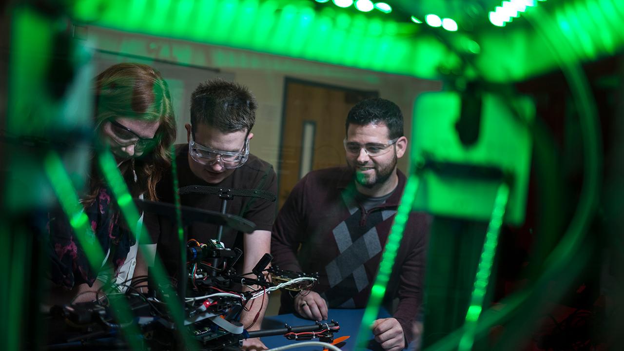 三名学生，两男一女，正在NMT实验室里研究无人机.